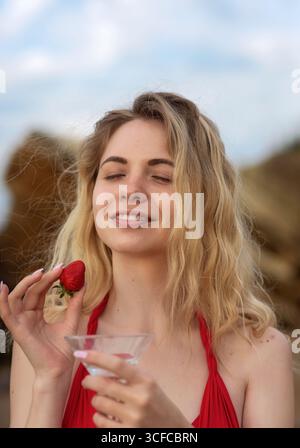 Die fröhliche Blondine hält rote Erdbeere in der Hand. Stockfoto