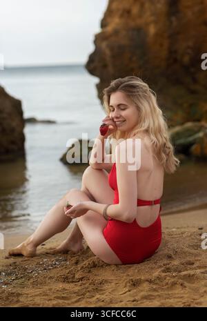 Fröhliche Blondine, die rote Erdbeere hält. Sie lacht am Sandstrand Stockfoto