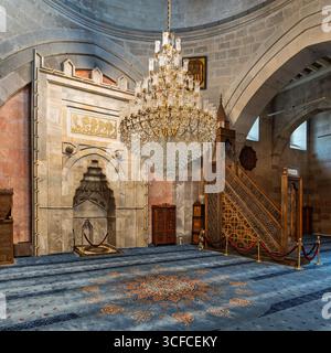 Das atemberaubende Innere der Kayseri Grand Moschee, türkisch: Ulu Camii, in Kayseri, Türkei. Mit dem kunstvollen Mihrab, der aufwändig geschnitzten Minibar und dem großen Kristallleuchter über gemustertem blauen Teppich Stockfoto