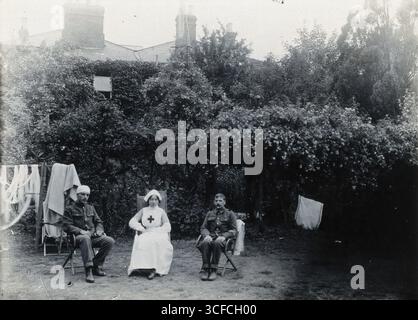 Holmleigh Auxiliary Military Hospital, Egge: Eine Krankenschwester und zwei Soldaten, von denen einer einen Verband auf dem Kopf hat, sitzen auf Liegestühlen in einem Garten mit Blütenbäumen im Hintergrund, um 1922. Stockfoto