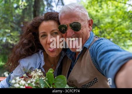 Ein wunderschönes und harmonisches Paar mittleren Alters macht ein lustiges Selfie, um im Freien Gesichter zu machen Stockfoto