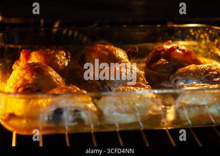 Frisch gebackene Hähnchenschenkel in einer Glasschale, die unter dem warmen Glühen des Ofens brutzelt, perfekt für ein köstliches Familienessen. Stockfoto