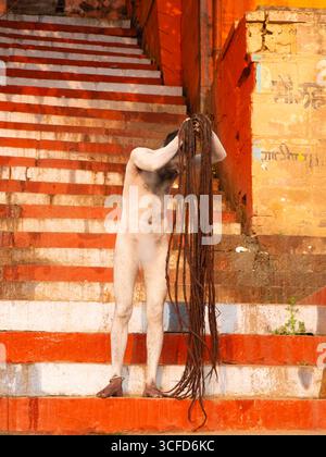 Naga Sadhu (hinduistischer Asket), bedeckt mit heiliger Asche (Bhasma), arrangiert seine Dreadlocks auf den Varanasi-Ghats. Stockfoto