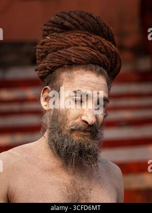 Naga Sadhu (hinduistischer Asket), bedeckt mit heiliger Asche (Bhasma), arrangiert seine Dreadlocks auf den Varanasi-Ghats. Stockfoto