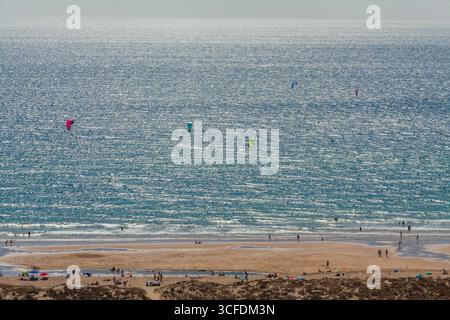 Eine weite, hochwinklige Landschaftsaufnahme eines bevölkerten Sandstrandes mit einem riesigen, schimmernden blauen Meer und mehreren Kitesurfern unter klarem Himmel Stockfoto