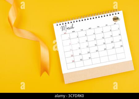 Schreibtischkalender März 2026 mit gelbem Band auf gelbem Hintergrund, Flat Lay. Stockfoto