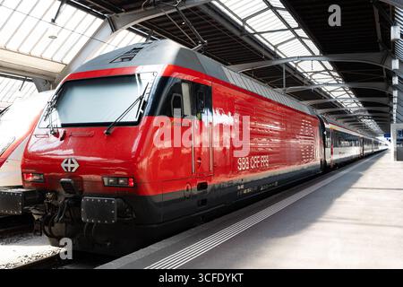 Zürich, Schweiz, 19. August 2025. Geparkte, rote Lokomotive eines Personenzuges im Erdgeschoss des Hauptbahnhofs. Weitwinkelansicht, Metall A Stockfoto