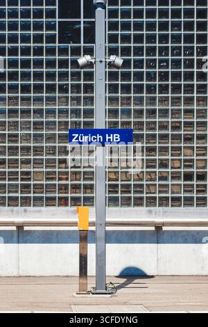 Zürich, Schweiz, 19. August 2025. Zürich HB Hauptbahnhof weiß auf blauem Schild an einem Pfosten in der Nähe eines ebenerdigen Bahnsteigs. Nahaufnahme, Metallzaun bac Stockfoto