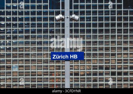 Zürich, Schweiz, 19. August 2025. Zürich HB Hauptbahnhof weiß auf blauem Schild an einem Pfosten in der Nähe eines ebenerdigen Bahnsteigs. Nahaufnahme, Metallzaun bac Stockfoto