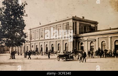 Parma, Italien, um 1910 (gestempelt 1925): Eine alte schwarz-weiße Postkarte mit dem Bahnhof (Stazione di Parma). Das Foto, das Anfang der 1900er Jahre aufgenommen wurde, zeigt den Übergang von Pferdekutschen zu frühen Autos, während die Postkarte Mitte der 20er Jahre verschickt wurde. Stockfoto