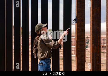 Santa Teresa, Usa. August 2025. Homeland Security Secretary Kristi Noem, verwendet eine Malerwalze, um schwarze Farbe auf die US-mexikanische Grenzmauer aufzutragen, auf Befehl von Präsident Donald Trump, 19. August 2025 in Santa Teresa, New Mexico. Quelle: TIA Dufour/CBP Photo/Alamy Live News Stockfoto