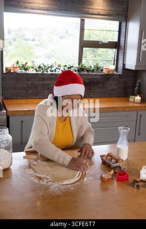 Ältere asiatische Frau im Weihnachtsmann hat Keksenteig auf der Küchenarbeitsplatte zu Hause mit Pin gerollt Stockfoto