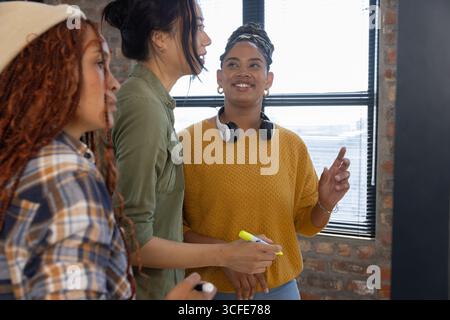 Verschiedene weibliche Kollegen arbeiten an Projekten im Loft Office mit gelben und weißen Markierungen zusammen Stockfoto