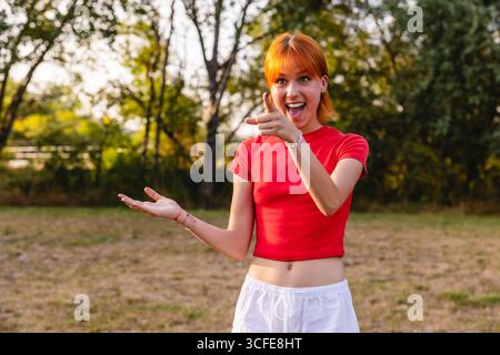 Aufgeregte junge Frau, die mit offener Hand im Park zeigt Stockfoto