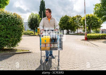 Bayern, Deutschland - 22. August 2025: Ein Mann schiebt einen Einkaufswagen mit Lebensmitteln über den Parkplatz eines Supermarktes *** ein Mann schiebt einen Einkaufswagen mit Lebensmitteln über den Parkplatz eines Supermarktes Stockfoto