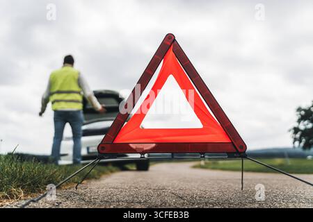 Bayern, Deutschland - 22. August 2025: Symbolisches Bild einer Panne: Ein Mann steht verzweifelt mit geöffneter Motorhaube vor seinem Auto. Das Warndreieck ist aufgebaut *** Symbolbild Autopanne: Ein Mann steht verzweifelt vor seinem Auto mit geöffneter Motorhaube. Das Warndreieck ist aufgestellt Stockfoto