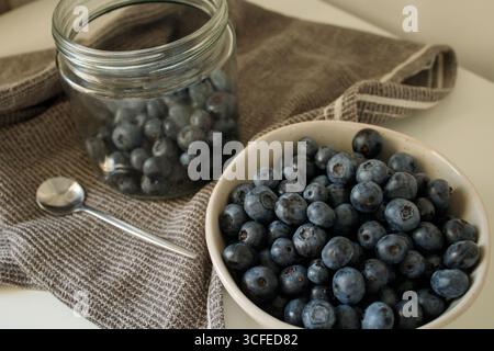 Frische Heidelbeeren in der Schüssel und im Glasgefäß auf dem Küchentisch Stockfoto