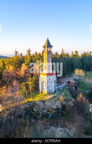 Der Stepanka Aussichtsturm steht hoch vor einem klaren Frühlingshimmel in Korenov, umgeben von üppigem Grün. Sonnenlicht beleuchtet den Turm und unterstreicht seine architektonische Schönheit. Stockfoto