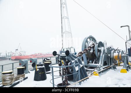Das Anlegedeck eines Frachtschiffes mit Ankerwinden, einer Ankerkette an Winden, Pollern und Haws mit Anlegeseilen, gefroren und mit Schnee bedeckt. Sn Stockfoto
