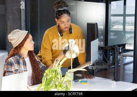 Verschiedene weibliche Kollegen arbeiten über silbernen Laptop am Schreibtisch mit Haftnotizblock zusammen Stockfoto