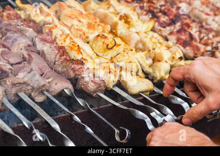 Die Hände des Mannes braten einen Schaschlik auf dem Grill. Schweinefleisch, Huhn und Lammfleisch auf Spießen auf dem Grill. Stockfoto