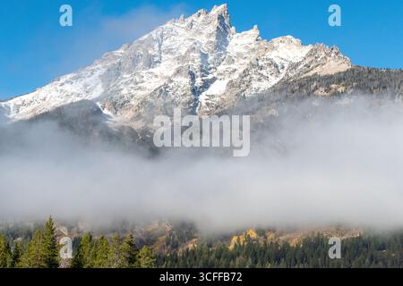 Der schneebedeckte Grand Teton Mountain erhebt sich über dem Nebel und Nebel und dominiert den Hintergrund vor einem blauen Himmel im Grand Teton National Park Stockfoto