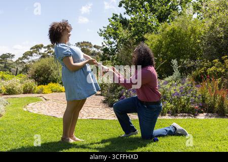 Diverse Paare knieten auf dem Gartenrasen neben dem geschwungenen Weg mit den Händen in der Nähe des offenen Ringkastens Stockfoto