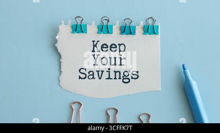 Home Office Arbeitsplatz mit Tastatur, Zwischenablage und Stift mit Text HALTEN SIE IHRE EINSPARUNGEN auf weißem Holzhintergrund , Business Stockfoto