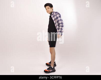 Junger Mann posiert lässig in trendigem Outfit vor einem schlichten Hintergrund Stockfoto