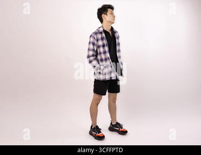 Junger Mann posiert lässig in trendigem Outfit vor einem schlichten Hintergrund Stockfoto