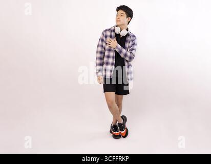 Junger Mann, der mit Kopfhörern steht und vor einem schlichten Hintergrund lächelt Stockfoto