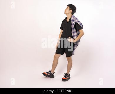 Junger Mann posiert lässig in trendigem Outfit vor einem schlichten Hintergrund Stockfoto