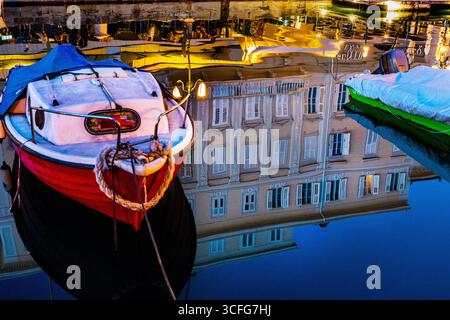 Historischer neoklassizistischer Palast spiegelt den Canal Grande in Triest, Italien, während ein kleines Boot den Weg beleuchtet. Stockfoto