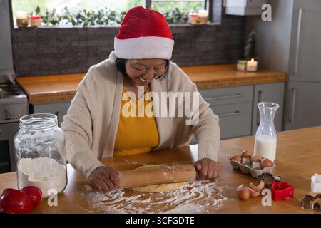Ältere asiatische Frau, die auf der Kücheninsel Teig mit Plätzchenschneidern für Urlaub platt macht Stockfoto