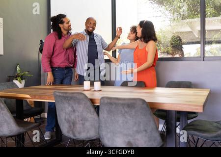 Verschiedene Kollegen, die lächeln und ihre Arme ausstrecken, umarmen den Tisch im Besprechungsraum, Kerzen Stockfoto