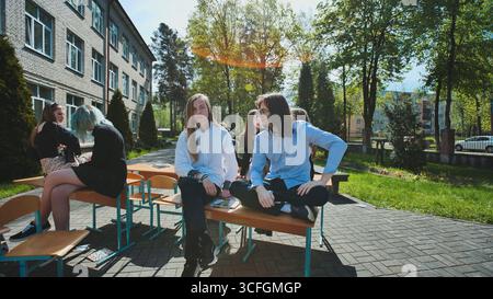 Die Schüler der High School machen eine Pause im Freien, entspannen sich auf den Schultischen und plaudern in der Sonne Stockfoto