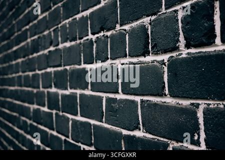 Eine markante schwarze Ziegelwand mit weißem Mörtel in einer detaillierten Nahansicht in Perspektive. Eine Nahaufnahme einer dunklen Ziegelmauer mit weißem Mörtel, Perf Stockfoto