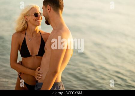 Sonnenküsste Paare teilen ein Lächeln und zärtliche Momente am Wasser während des Sonnenuntergangs und fangen das Wesen der Sommerromantik und des Glücks ein. Stockfoto