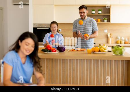 In einer hellen Küche jonglieren zwei Freunde spielerisch mit Obst und bereiten frische Zutaten vor, um eine lebendige Atmosphäre voller Freundschaft und Spaß zu schaffen. Stockfoto