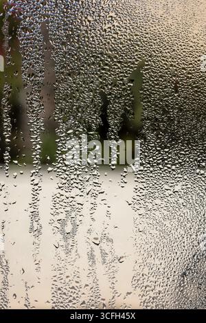 Makroansicht von Wassertröpfchen und kondensierter Feuchtigkeit, die abstrakte Streifen auf einer vertikalen Glasoberfläche bilden. Stockfoto