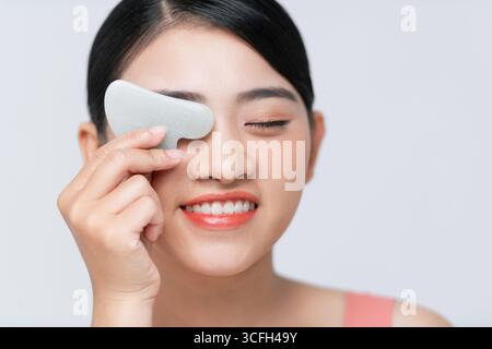 Porträt einer hübschen jungen Dame, die Gua-Sha-Steinkratzer benutzt, während sie Hautpflegeprogramme macht. Stockfoto
