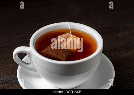 Teebeutel in weißer Tasse mit heißem Wasser auf Holztisch, Nahaufnahme Stockfoto