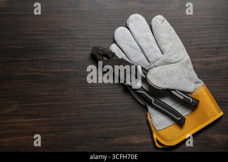 Metallzange und Sicherheitshandschuhe aus Leder auf Holztisch, Draufsicht, Kopierraum, Nahaufnahme Stockfoto