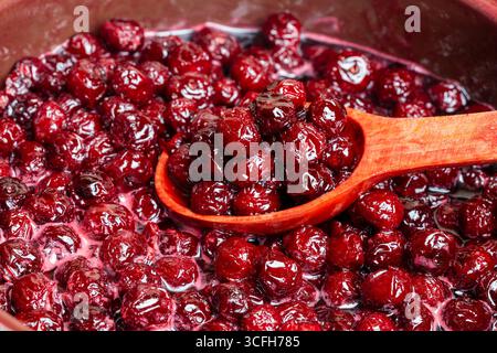 Zubereitung frisch gepflückter roter Kirschen mit Zucker zu Kirschmarmelade in einem Topf mit einem Holzlöffel, Nahaufnahme. Kochen Beeren Marmelade, hausgemachte Kekse Stockfoto