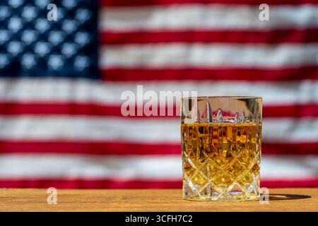 Glas Whiskey auf Holztisch vor dem Hintergrund einer amerikanischen Flagge, Nahaufnahme. Bourbon, ein amerikanischer Whiskey, wird oft mit dem United in Verbindung gebracht Stockfoto