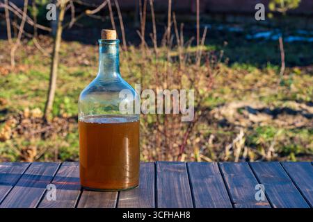 Glas große Flasche mit hausgemachtem Wein auf einem Holztisch neben dem Garten an einem sonnigen Tag, Nahaufnahme, draußen Stockfoto