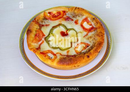 Hausgemachte leckere Pizza mit Tomaten und Käse auf einer weißen Keramikplatte, auf einer hellen Holzoberfläche. Stockfoto