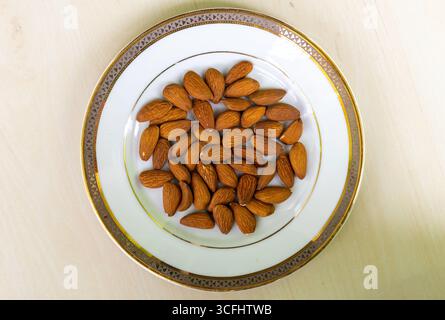 Draufsicht auf Mandelnüsse auf weißer Platte auf hölzernem Hintergrund. Mandeln sind reich an Nährstoffen, einschließlich Ballaststoffen, Magnesium, Vitamin E, Kalzium, Phosphor Stockfoto