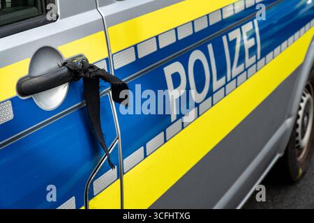 Landkreis Osnabrück, Deutschland 23. August 2025: Im Bild: Am Türgriff eines deutschen Polizeifahrzeugs mit blauer und gelber Beklebung ist ein schwarzer Trauerflor befestigt. Das Band steht als stilles Symbol für Trauer, Gedenken und Respekt gegenüber verstorbenen Kolleginnen und Kollegen oder Opfern von Gewalttaten. Der schwarze Flor am Streifenwagen macht deutlich, dass die Polizei nicht nur für Sicherheit und Ordnung im Straßenverkehr und im öffentlichen Raum steht, sondern auch Anteilnahme zeigt und Solidarität nach außen tragen. In solchen Momenten wird das Einsatzfahrzeug mit seinem refl Stockfoto