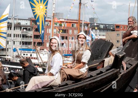 Amsterdam Niederlande 23. August 2025 Tausende säumen die Küste von Het ij und den Hafen von Amsterdam für das fünfjährliche Sail Tall Ships Event. Zwei Damen in mittelalterlicher Tracht lächeln von der Kamper Kogge eine Rekonstruktion eines Zahnrads, das im 14. Jahrhundert zwischen Handelsstädten im Norden Europas segelte. HAVEN, Sail25, People, Niederländisch, Nederland, Holland, Besucher, Stockfoto